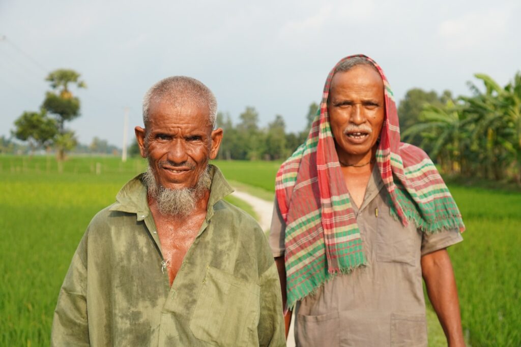 A moment of shared joy and satisfaction is captured as two farmers stand together in a field, their faces lit up with genuine smiles.
