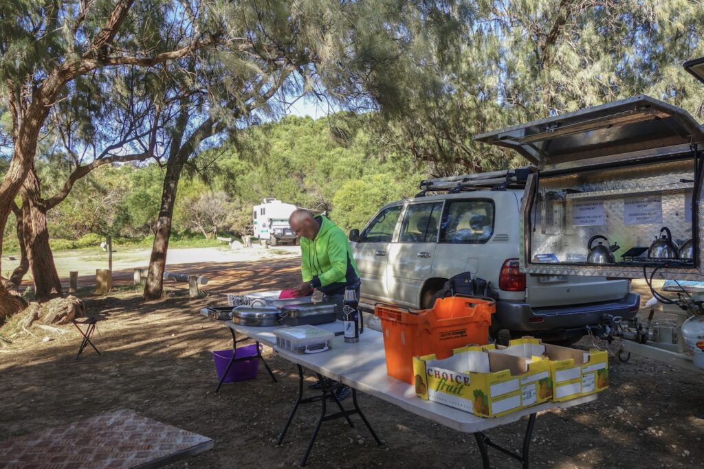Man preparing items at an outdoor table beside a vehicle.